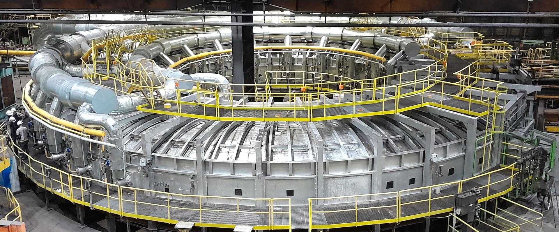 Drehherdofen im Werk Zeithain. Kreisförmiger Drehherdofen in einer Werkhalle des Mannesmannröhren-Werks Zeithain, umgeben von gelben Laufstegen und Rohrleitungen.