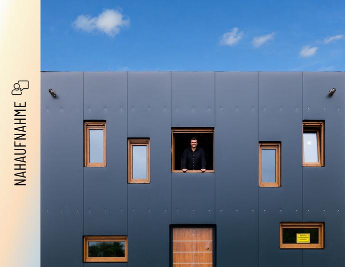 Christoph Jenner schaut aus einem Fenster der anthrazitfarbenen Stahlfassade Christoph Jenner schaut aus einem Fenster der anthrazitfarbenen Stahlfassade seines Green Steel Home .